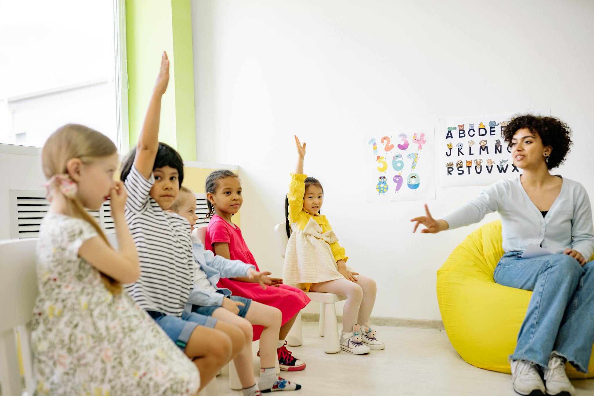 Children raising hands in classroom with a teacher, learning and engaging.